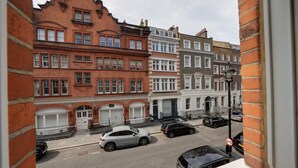 Vista de la calle con edificios de ladrillo rojo, coches aparcados y una señal de límite de velocidad.