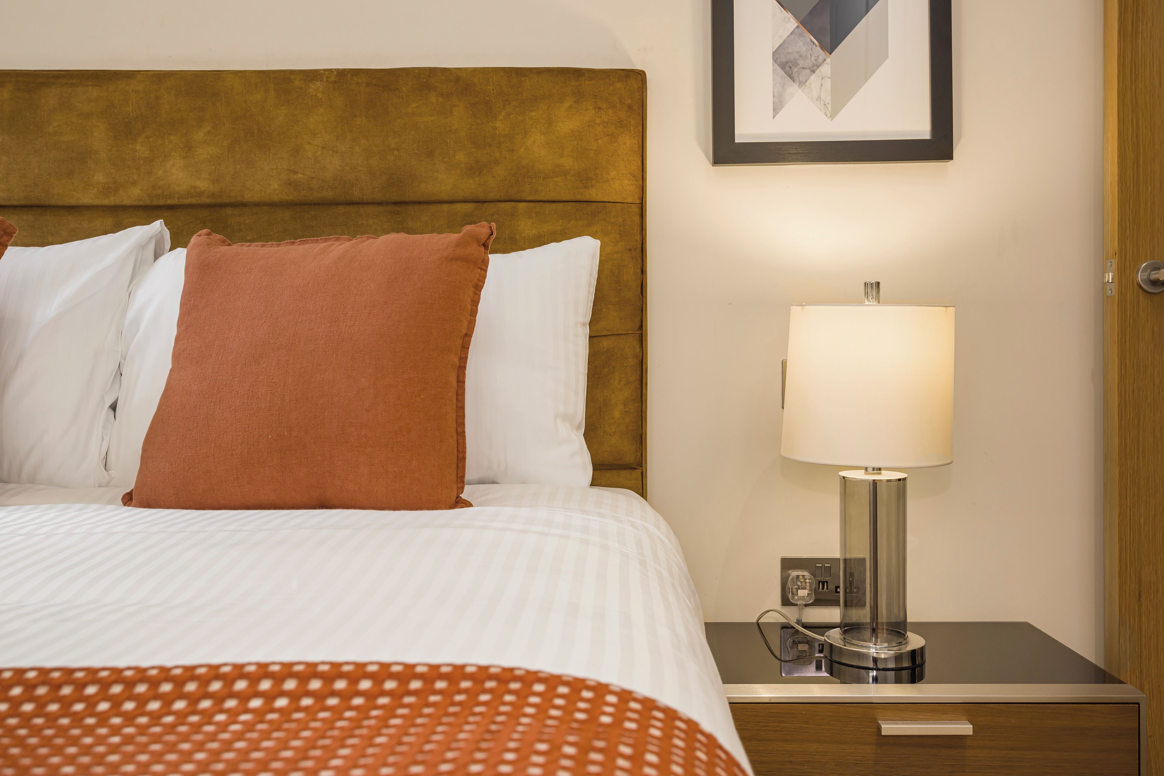 Una habitación de hotel con una cama, una mesita de noche, una lámpara y una puerta.