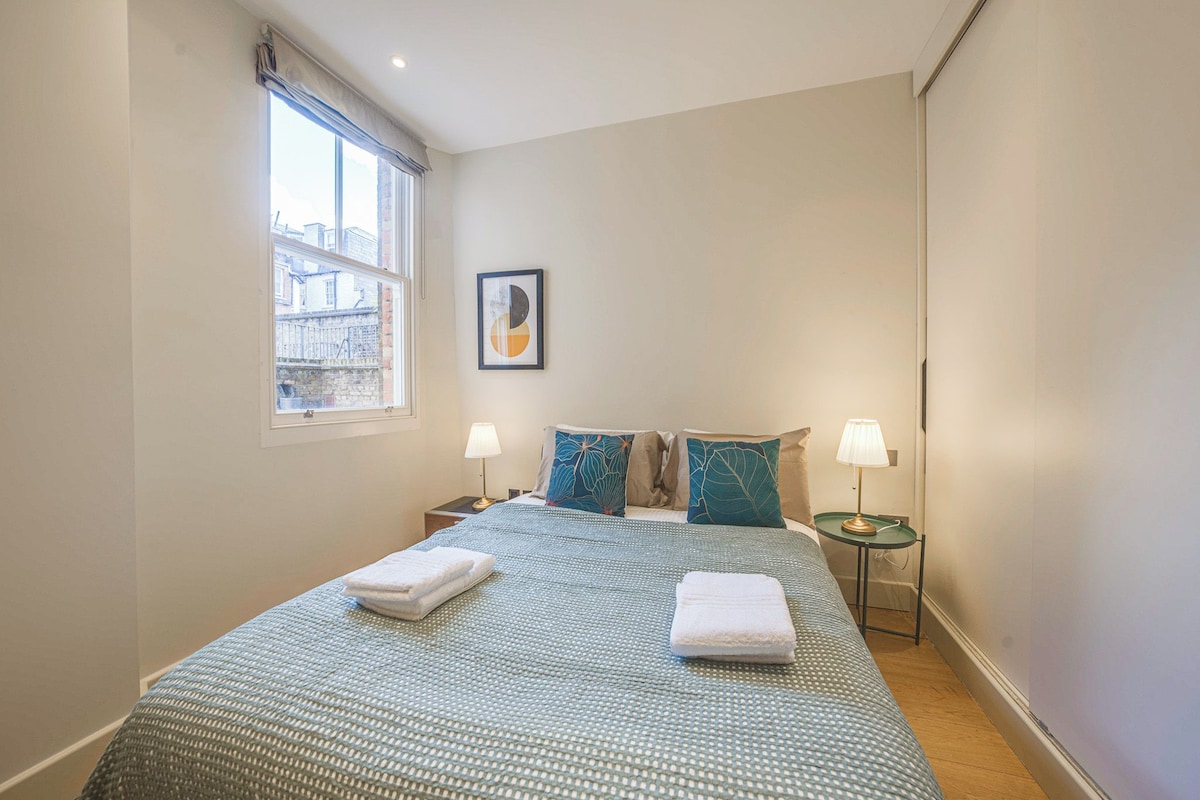 A hotel room with a large bed, two bedside tables, a window, and a framed picture on the wall.