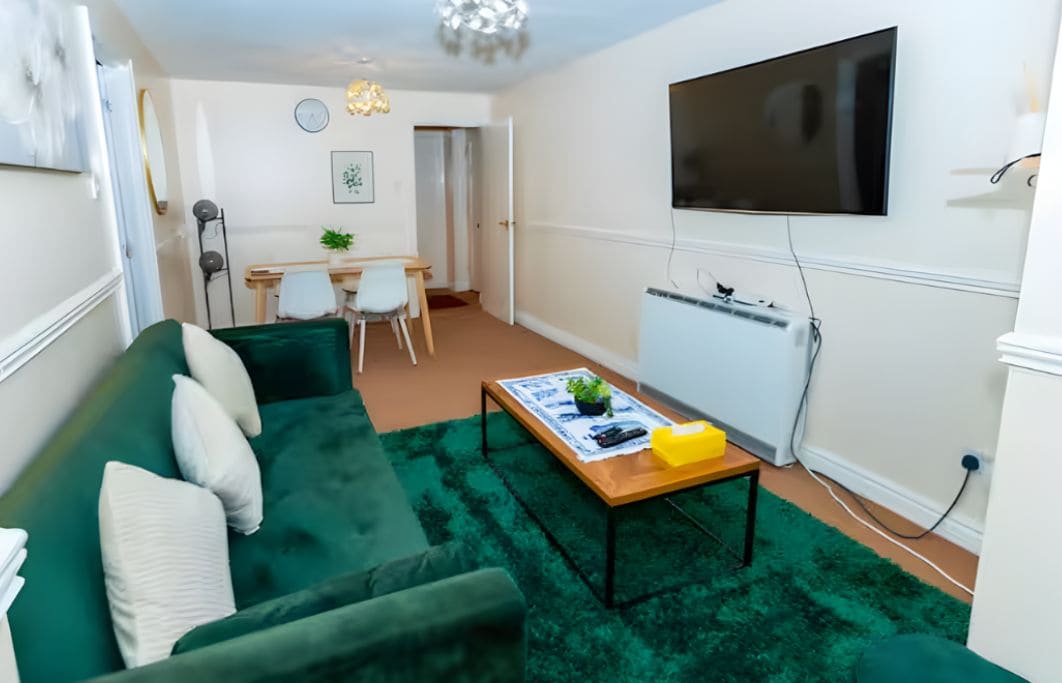 Una sala de estar con un sofá verde, una mesa de centro y un televisor montado en la pared.