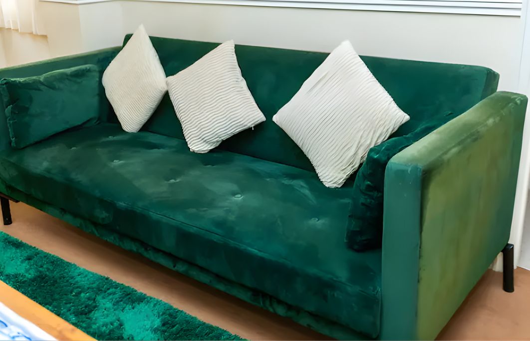 A green sofa with three white pillows.