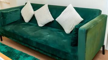 A green sofa with three white pillows.