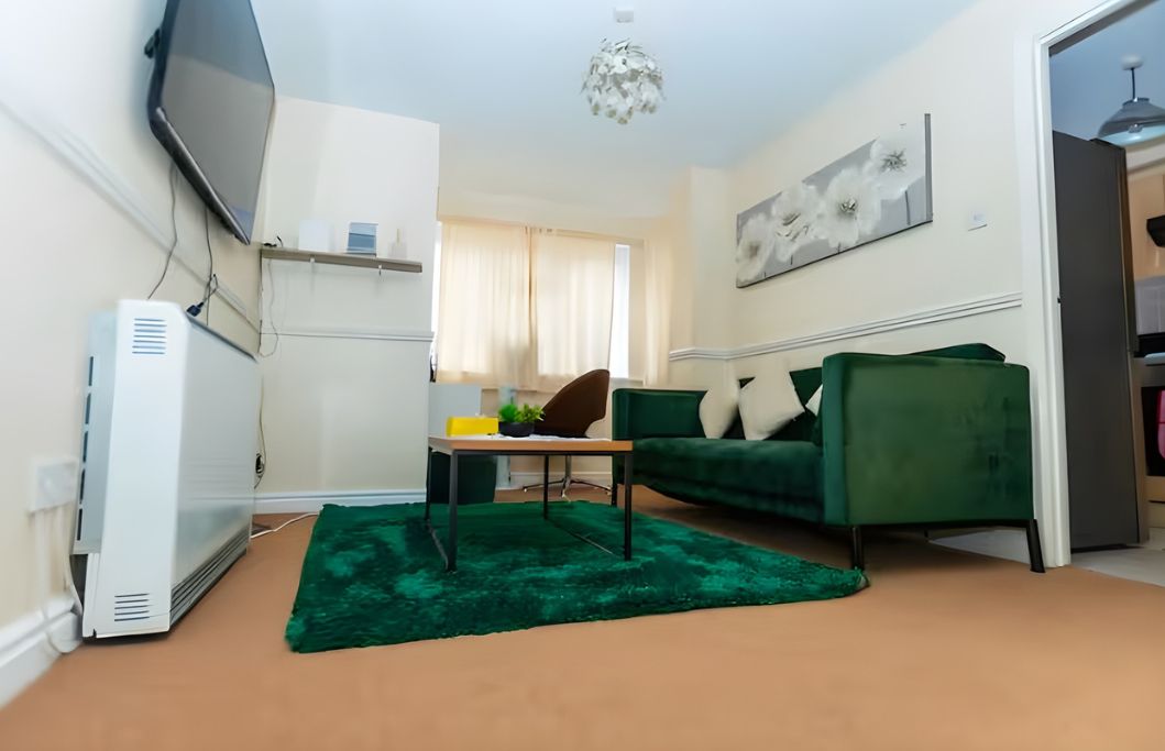 A living room with a green sofa, a small table, a TV, and a ceiling light.