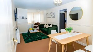 A modern living room with a green sofa, a wooden dining table, and a chandelier. - Cozy 1BR Ground Floor Maisonette in Town Centre (Bletchley)