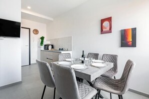 Un comedor moderno con una mesa rectangular dispuesta para seis personas, sillas grises tapizadas, un televisor de pantalla plana en la pared y obras de arte en las paredes.