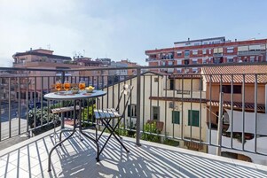 Un balcón con mesa y sillas, con vistas a un paisaje urbano lleno de edificios.