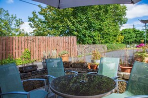 An outdoor patio with a round table and chairs, surrounded by potted plants and a wooden fence. - The Banking Hall -  a house  that sleeps 6 guests  in 2 bedrooms (Brightons)
