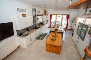 Une cuisine moderne avec des meubles blancs, un îlot central en bois et un coin repas agrémenté d’un rideau rouge.