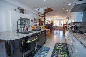 A modern kitchen with a central island, a spiral staircase, and a view into the dining area. - The Banking Hall -  a house  that sleeps 6 guests  in 2 bedrooms (Brightons)