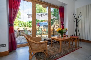 A room with a wicker chair, a wooden table, and a vase of flowers. - The Banking Hall -  a house  that sleeps 6 guests  in 2 bedrooms (Brightons)