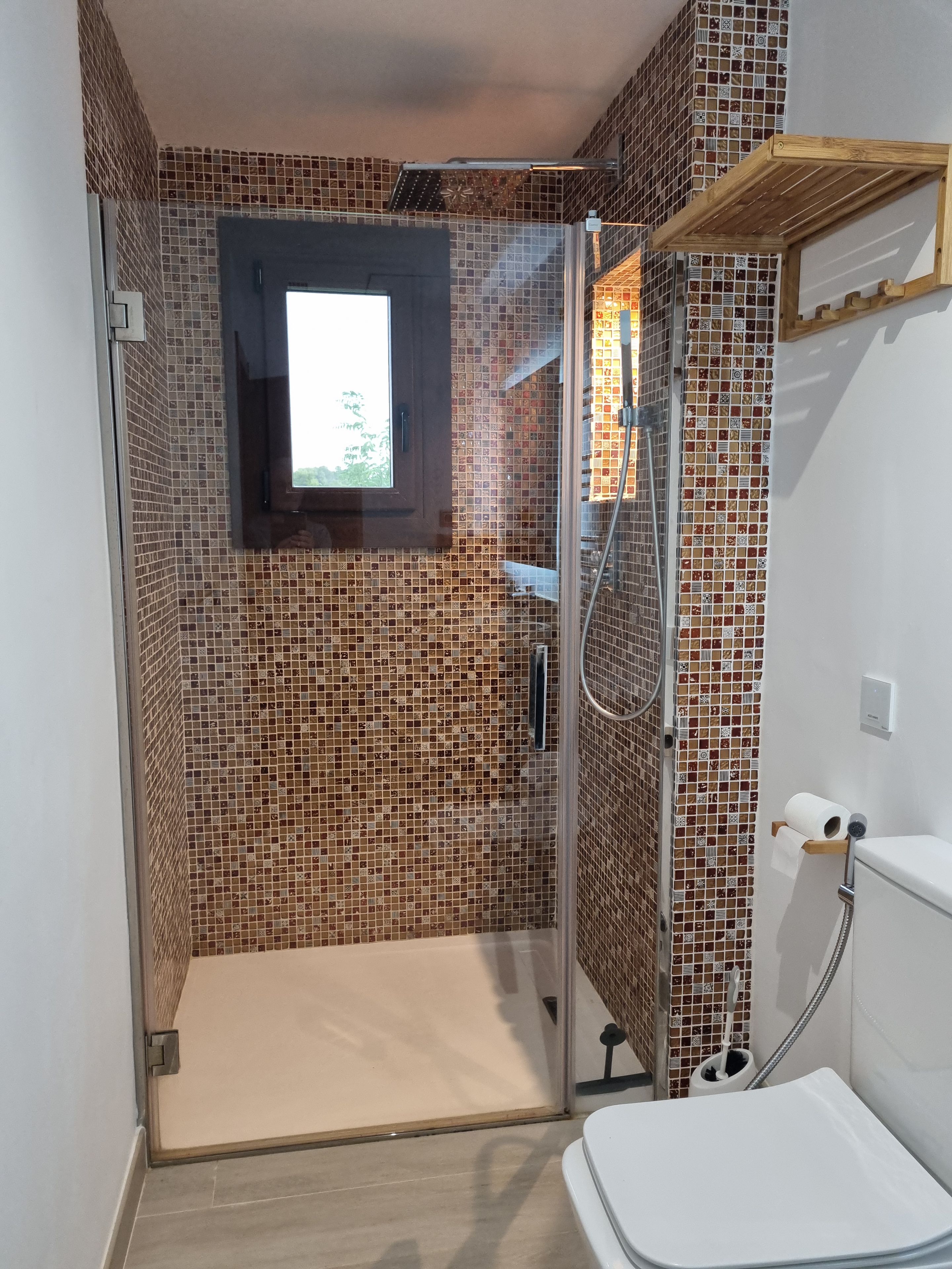 Een badkamer met een douche, toilet en een raam.