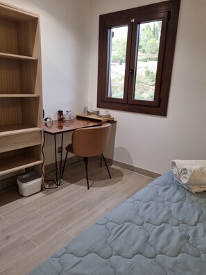 A room with a bed, a desk with a chair, a window, and a bookshelf.