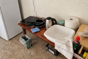 Un área de cocina con un lavamanos, una tetera, una sartén, un cubo de basura y una mesita con una toalla.