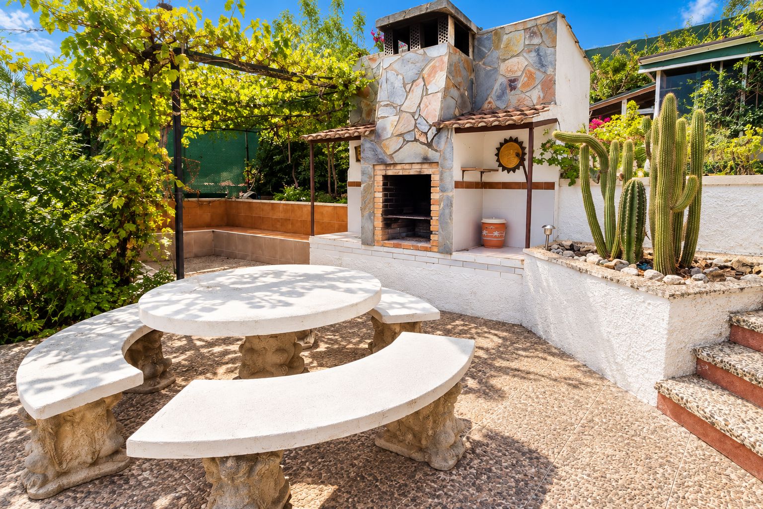An outdoor patio with a round table and benches, a stone wall, and a cactus garden.