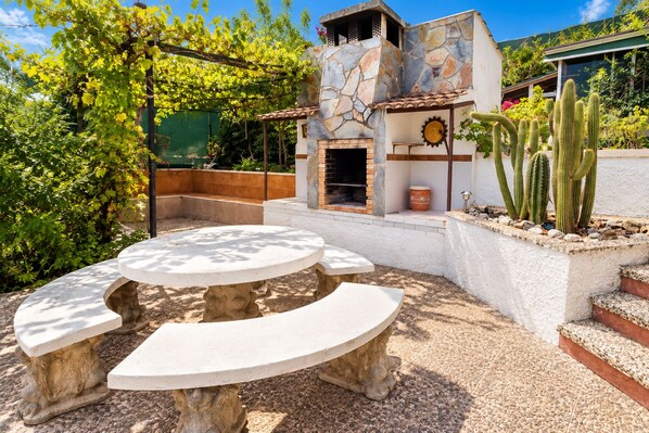 Un patio al aire libre con una mesa redonda y bancos, una pared de piedra y un jardín de cactus.
