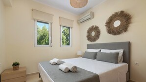 Un dormitorio ordenado con una cama, dos ventanas, una mesita de noche con una planta y decoración en la pared.