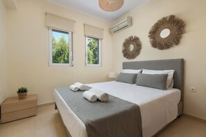 A neatly arranged bedroom with a bed, two windows, a bedside table with a plant, and decorative wall art. - Villa Olvia - Three Bedroom Villa, Sleeps 6 (Rhodes)