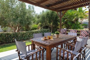 Une terrasse extérieure avec une table et des chaises en bois, entourée d’une végétation luxuriante et agrémentée d’une pergola.