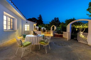 An outdoor patio with a round table and chairs, surrounded by white walls and a tiled floor. - Villa Amelie - One Bedroom Villa, Sleeps 4 (Ixia)