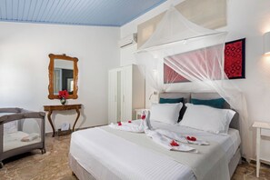 A hotel room with a large bed, a bedside table, a chair, a mirror, and a wall-mounted air conditioner. - Villa Amelie - One Bedroom Villa, Sleeps 4 (Ixia)