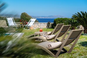 Poltronas de descanso ao ar livre com vista para o mar, uma parede de pedra e vegetação.