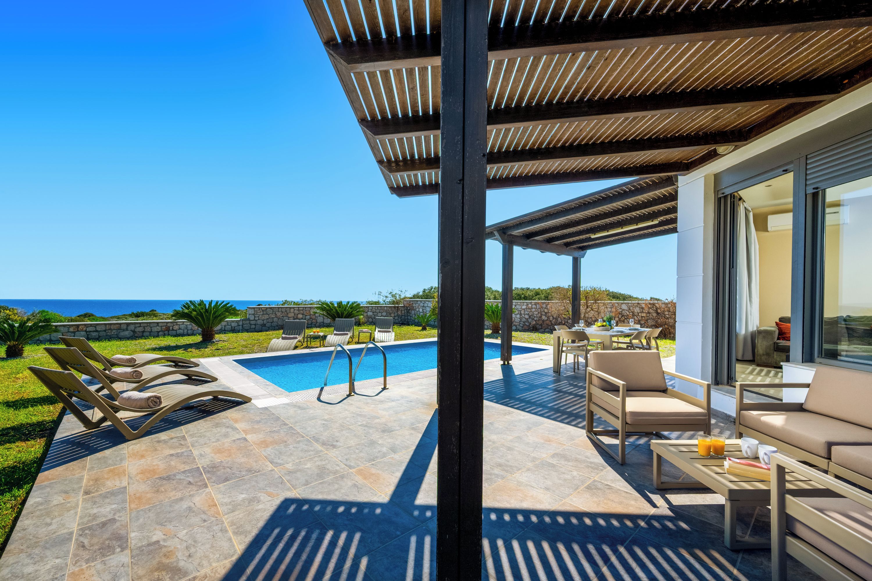 Ein überdachter Außenbereich mit Pool, Liegestühlen und einer Sitzecke mit Meerblick.