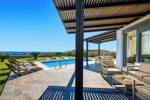 Un espace extérieur abrité comprenant une piscine, des chaises longues et un coin salon offrant une vue sur la mer.