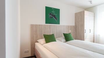 Una habitación de hotel con cama, almohadas verdes, cabecera de madera, cuadro con motivos verdes y una ventana con cortinas.