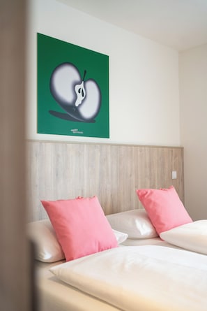 A hotel room with a bed, two pink pillows, a green wall with a fruit illustration, and a wooden headboard. - eeeden apartments Wien 10 (Vienna)