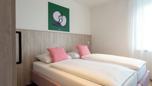 Cama doble con dos almohadas, cabecero de madera y pared verde con una obra de arte en forma de corazón.