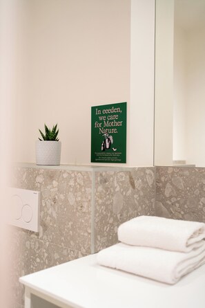 Un baño con un lavamanos blanco, una toalla, un letrero verde y una planta en maceta.
