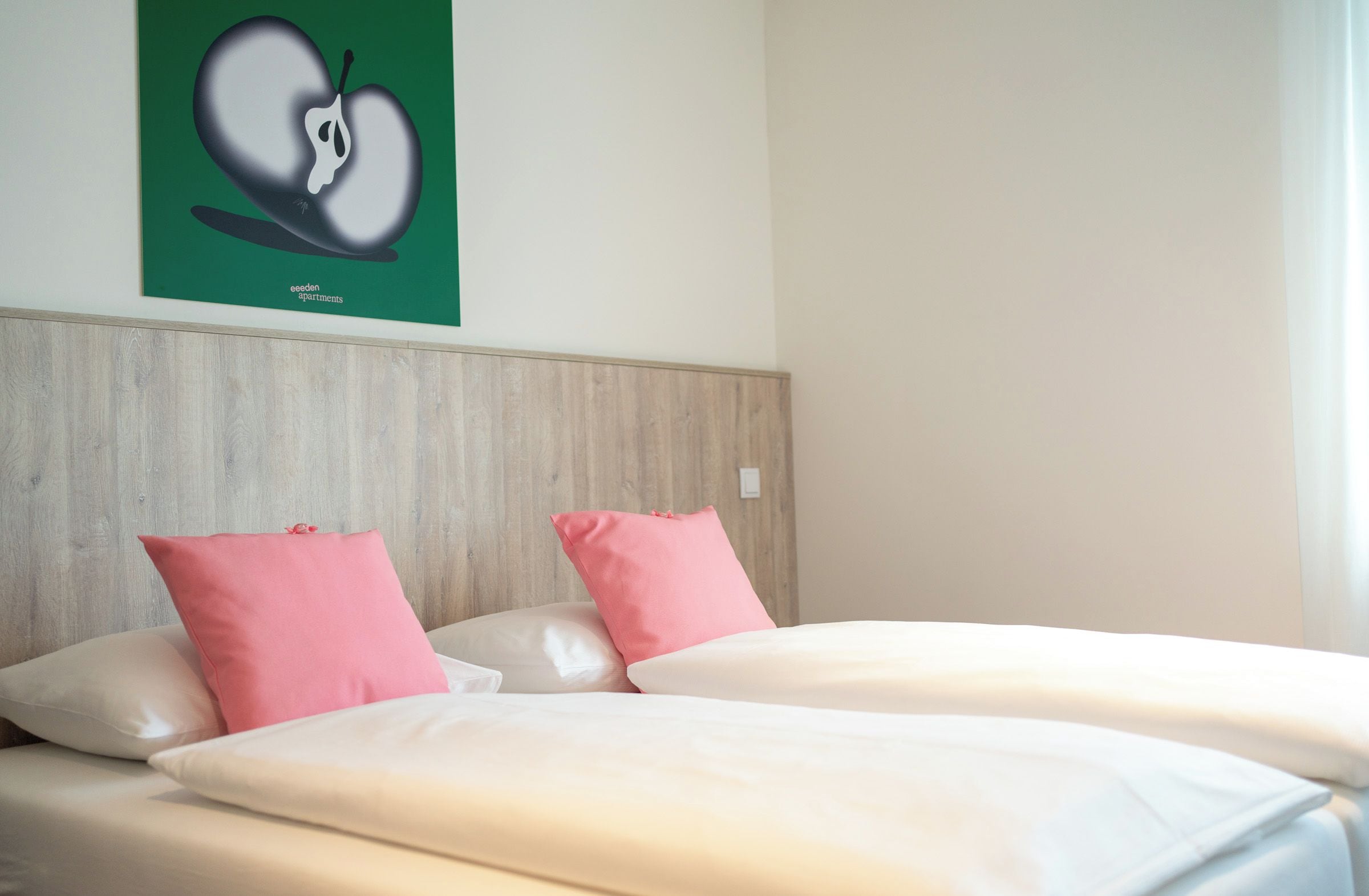 A hotel room with a bed, two pillows, a wooden headboard, and a green wall with a fruit illustration.