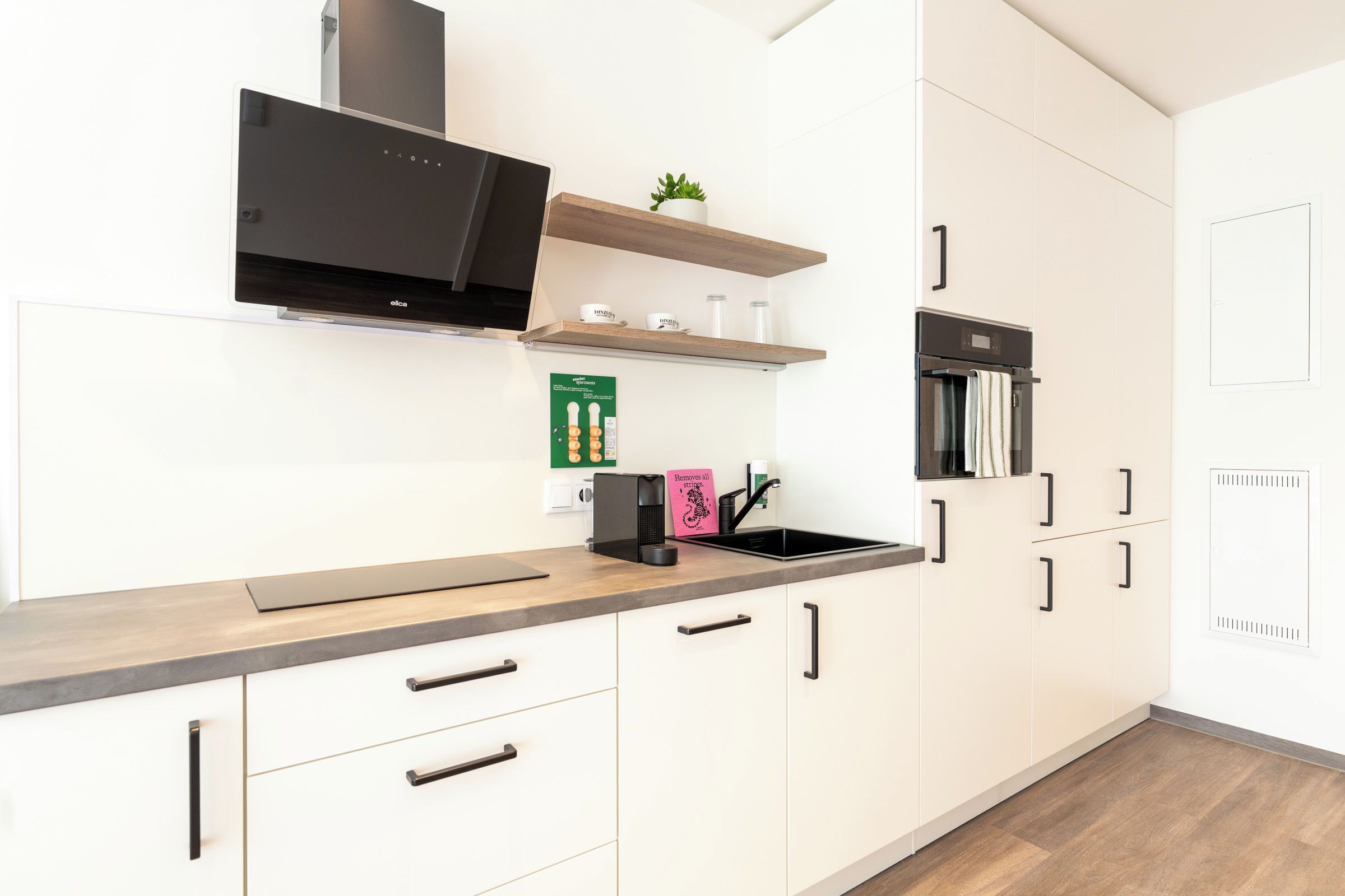 Una cocina moderna con armarios blancos, una campana extractora negra, horno empotrado y encimera con hervidor y cafetera.