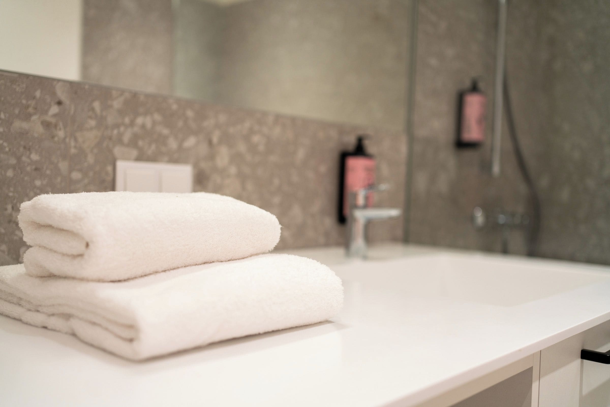A bathroom with a white countertop, a folded white towel, a mirror, and a shower area.