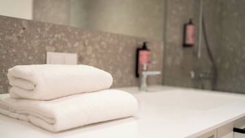 A bathroom with a white countertop, a folded white towel, a mirror, and a shower area.