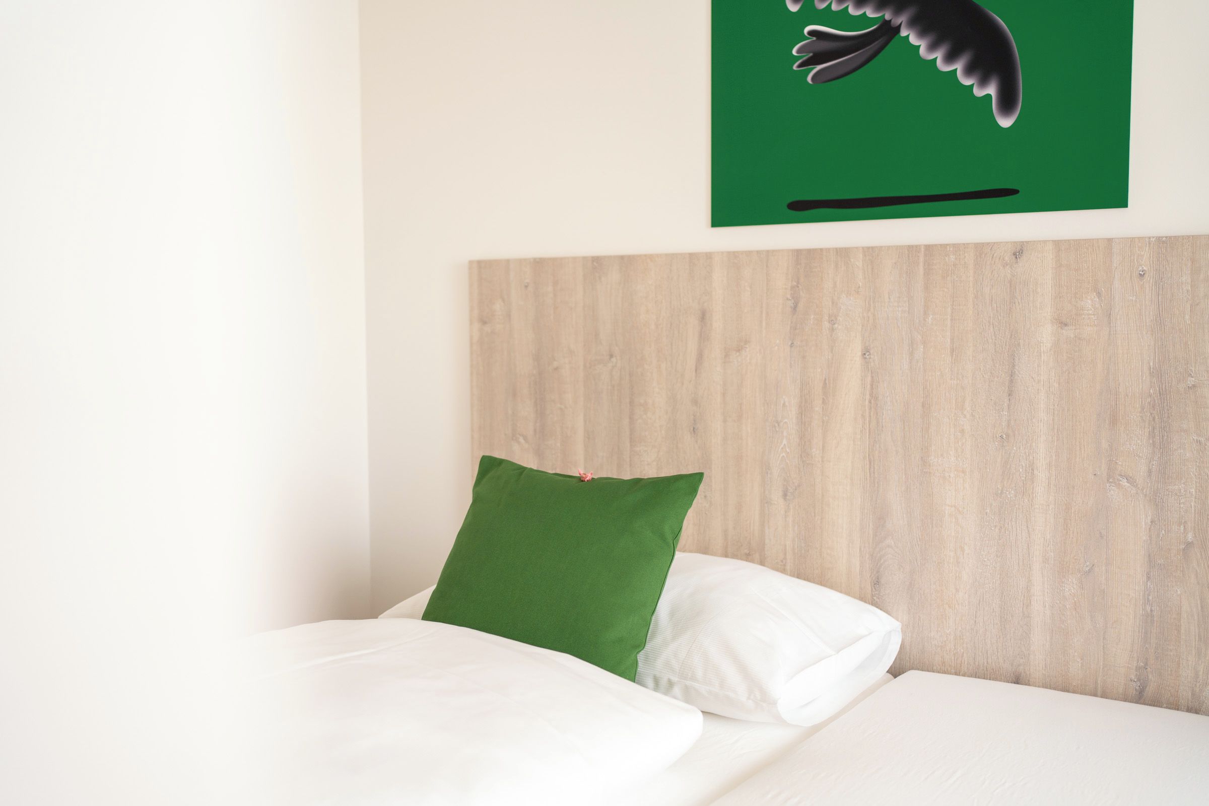 Un lit avec une literie blanche et un oreiller vert, adossé à une tête de lit en bois.