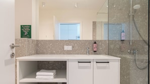 Un baño moderno con tocador blanco, cabina de ducha de vidrio y un cartel sobre sostenibilidad en la pared.