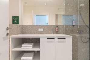 Um banheiro moderno com toucador branco, box de chuveiro em vidro e pôster sobre sustentabilidade na parede.
