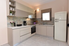A modern kitchen with a built-in oven, a refrigerator, and a window above the sink. - Mon Emvasia Margarites Villa A (Rethymno)