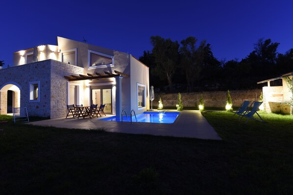 Une maison moderne dotée d’une piscine, d’un espace salon extérieur et d’une façade en pierre.