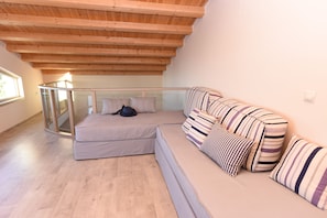 A modern loft bedroom with a wooden ceiling, a glass railing, a sofa, and striped pillows. - Mon Emvasia Margarites Villa A (Rethymno)