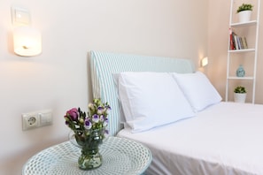A neatly made bed with white linens, a striped headboard, and a bedside table with a vase of flowers. - Mon Emvasia Margarites Villa A (Rethymno)