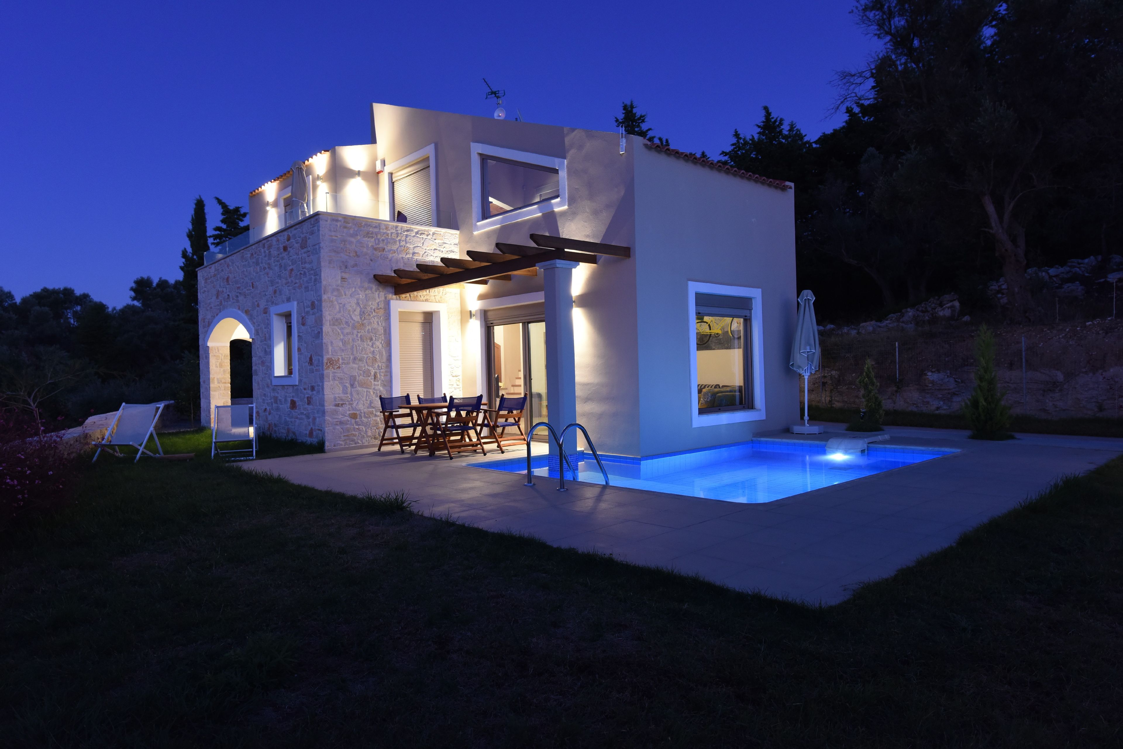A modern house with a swimming pool, outdoor seating, and a stone facade.