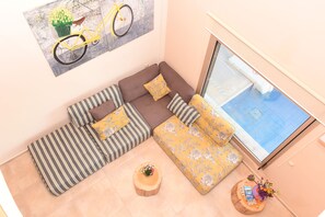 A modern living room with a sectional sofa, striped pillows, a round wooden coffee table, and a large window with a view. - Mon Emvasia Margarites Villa B (Rethymno)