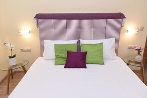 Ein Bett mit einem gestreiften Kopfteil, zwei Kissen und ein Glastisch mit einem Blumenstrauß.