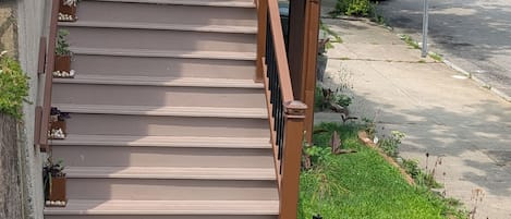 A set of outdoor stairs leading to a building entrance, surrounded by greenery and a sidewalk.