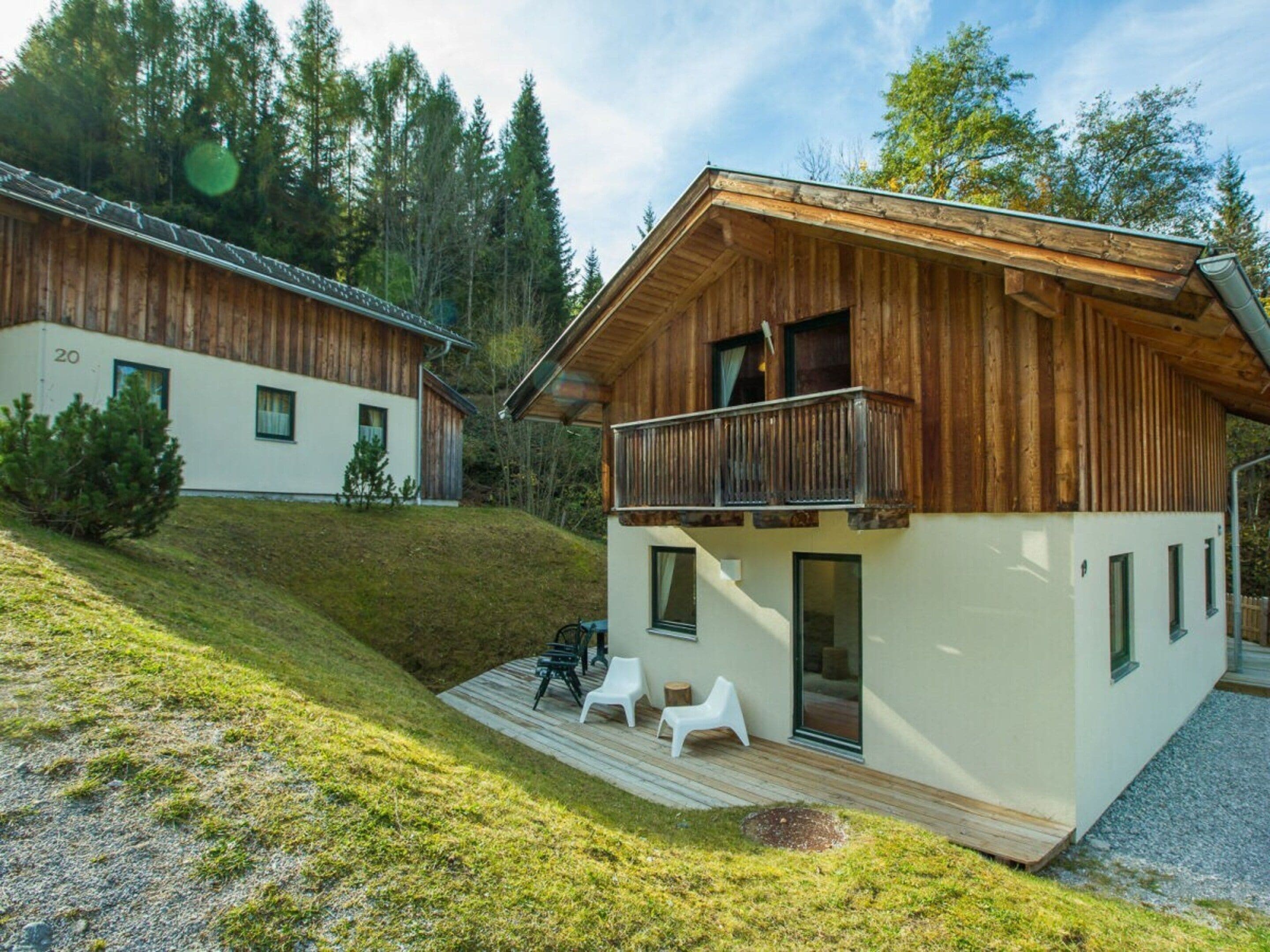 Une cabane en bois à deux étages, dotée d’un balcon, d’une terrasse avec mobilier d’extérieur et entourée d’une zone boisée.