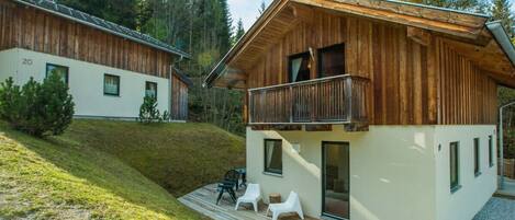 Een houten chalet met twee verdiepingen, een balkon, een terras met tuinmeubilair en een omliggend bosgebied.
