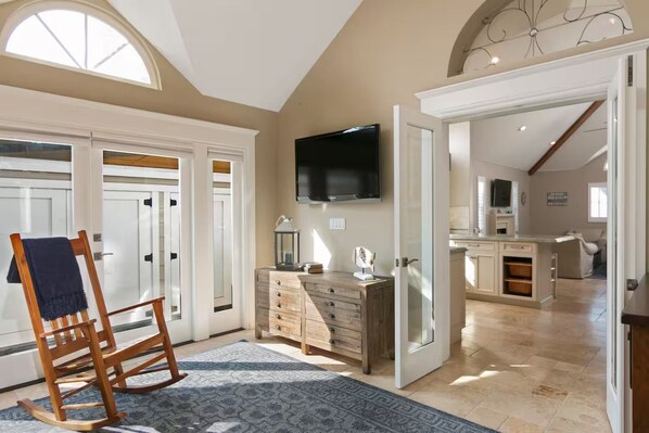 A spacious room with a large window, a wooden rocking chair, a flat-screen TV, and a kitchen area with cabinets and a countertop. - 25% Off Sept, Perfect For Families, Walk To Beach! (Ventura)