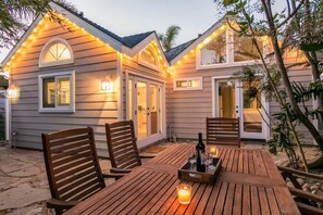 A patio with wooden furniture and a table set for dining, surrounded by a house with exterior lighting. - 25% Off Sept, Perfect For Families, Walk To Beach! (Ventura)